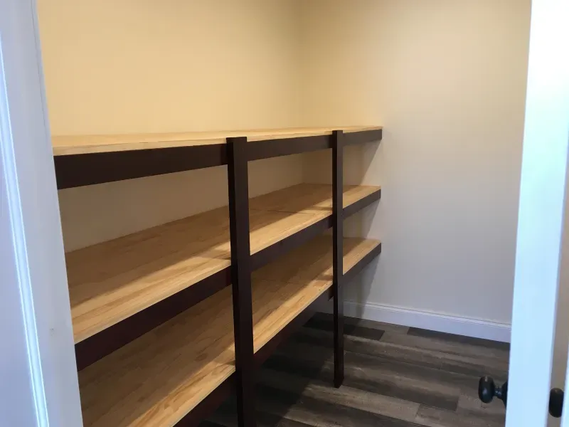 Empty wooden shelves in a small closet with dark metal supports and striped flooring.