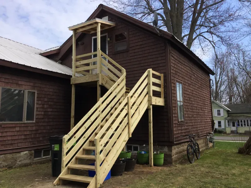 Brown house with an exterior wooden staircase and small porch under a cloudy sky