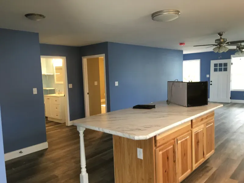 Empty blue kitchen and living space with an island, ceiling fan, and white front door