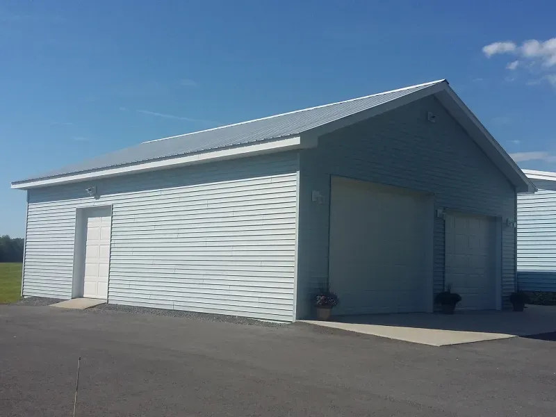 White metal storage building with a large garage door and side entrance on a paved lot under a blue sky