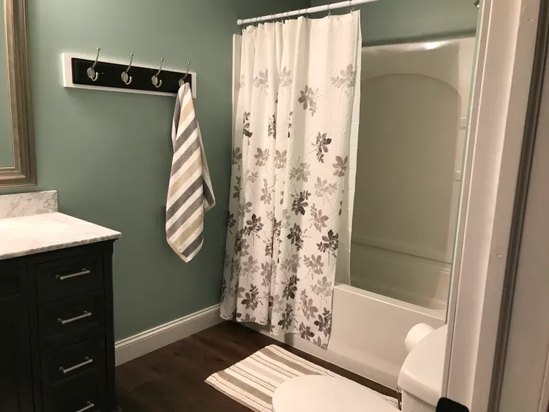 Bathroom with green walls, dark vanity, striped towel, and floral shower curtain beside a bathtub.