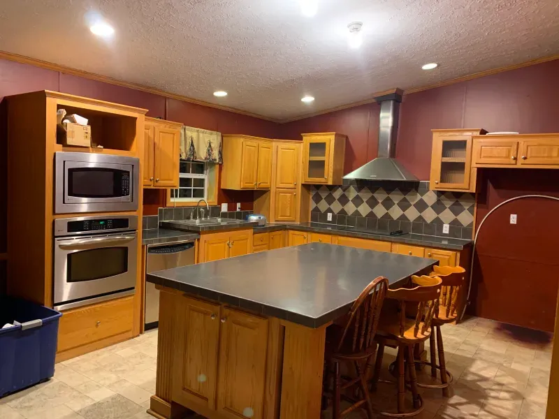 Modern kitchen with wooden cabinets, central island, double oven, and stainless range hood