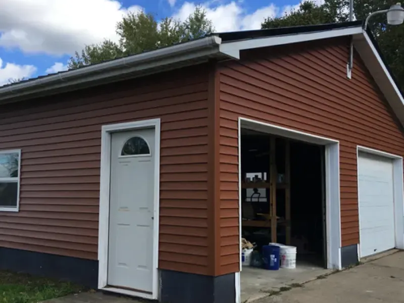 Brown garage with white doors and a small side entry door under a cloudy sky