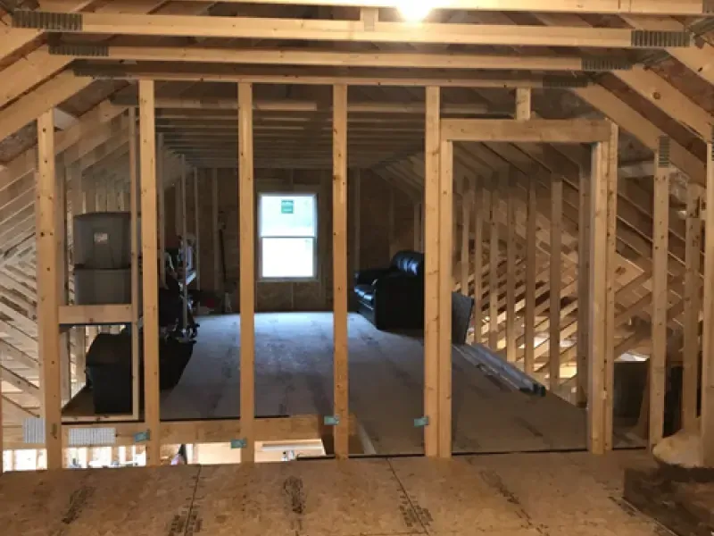 Unfinished attic with exposed wooden framing, open floor, and a window at the far end.