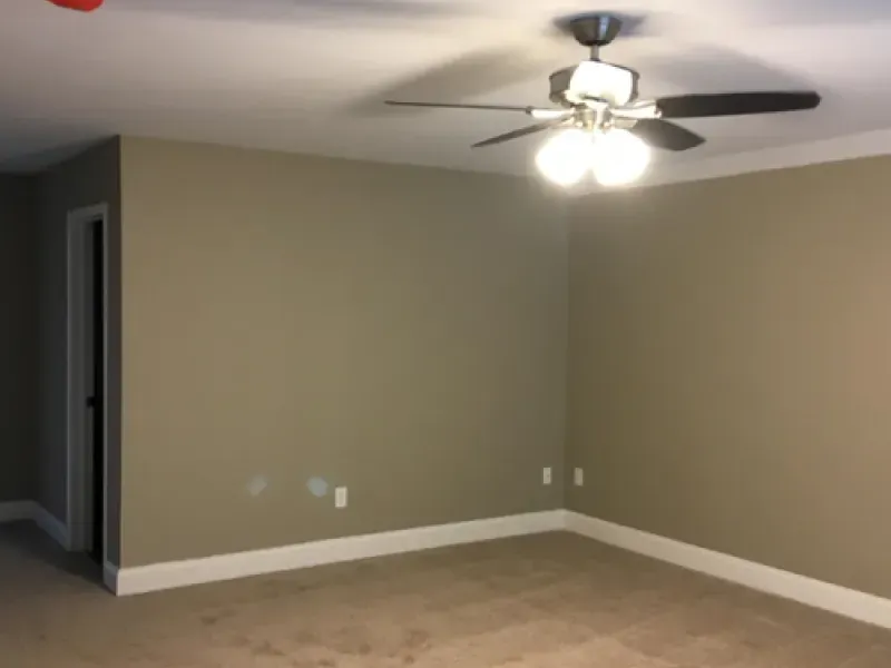 Empty beige living room with ceiling fan, white trim, and carpeted floor