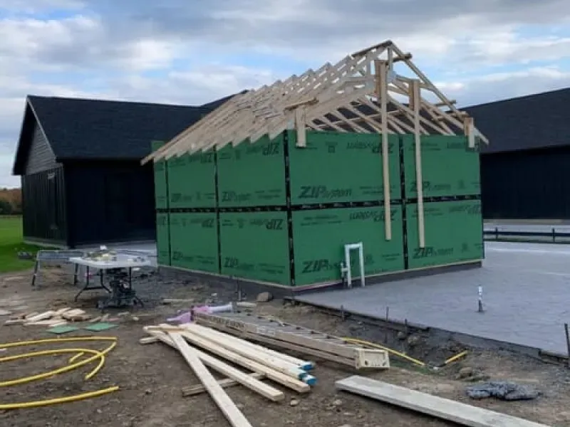 Partially built house with green wall panels and exposed roof framing on a construction site