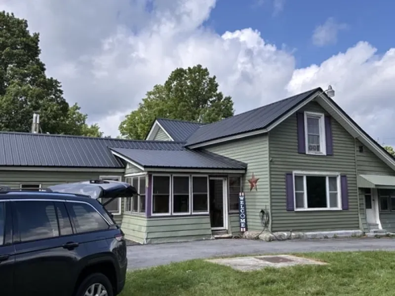 Green house with gray metal roof, white-trimmed windows, and parked SUV in the driveway.