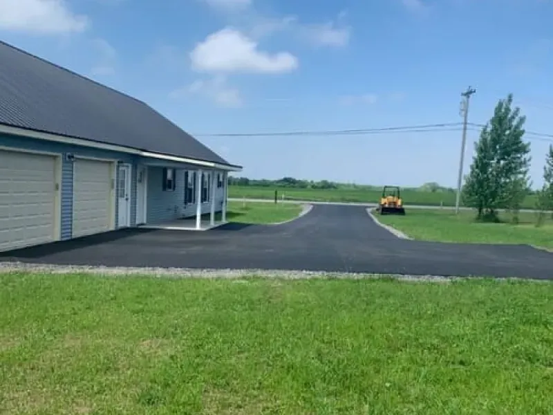 Building beside a freshly paved driveway and grassy field under a clear blue sky