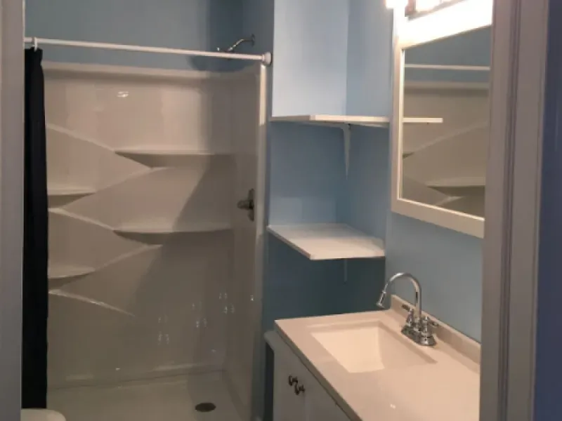 Small bathroom with a shower stall, sink, mirror, and blue walls.