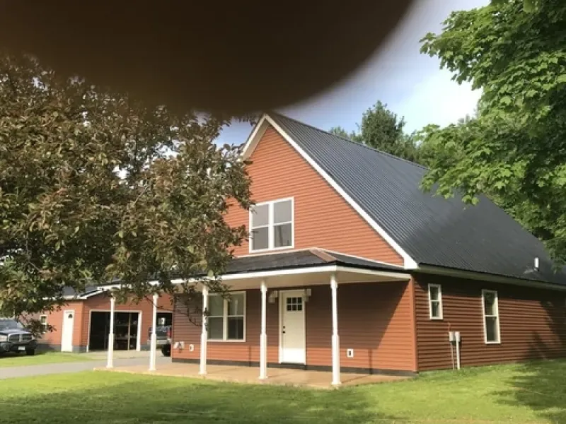 Orange house with a dark roof and white porch in a grassy yard, partly framed by trees