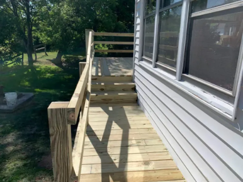 Wooden accessibility ramp with railings beside a house, leading to a small landing.