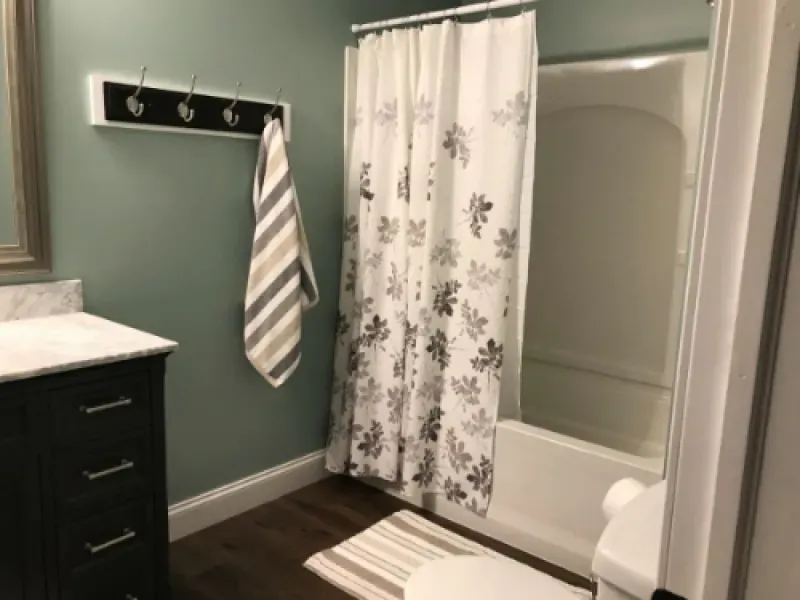 Bathroom with green walls, dark vanity, striped towels, floral shower curtain, and a white tub.