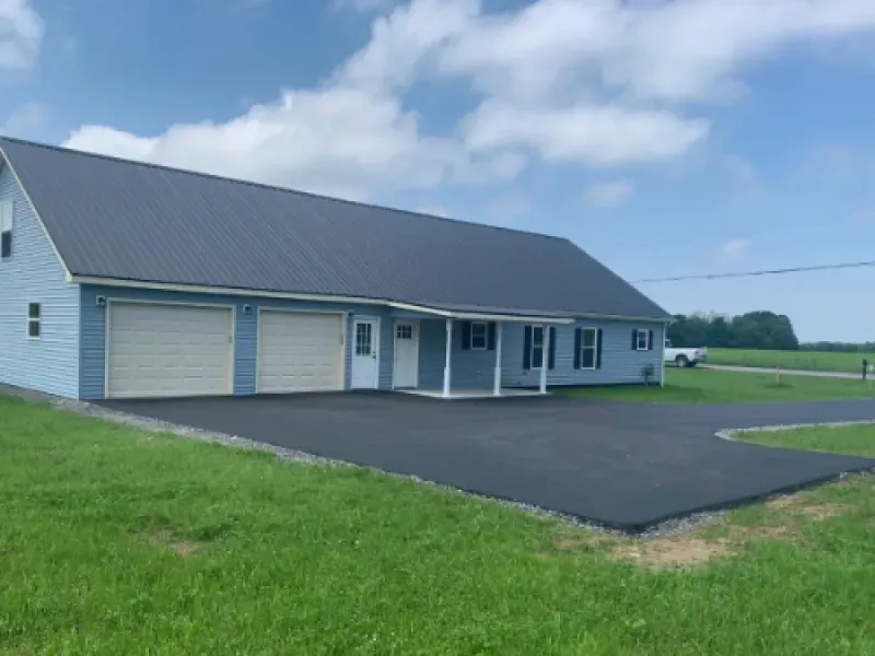 Single-story blue house with attached garage and dark roof beside a paved driveway and green lawn