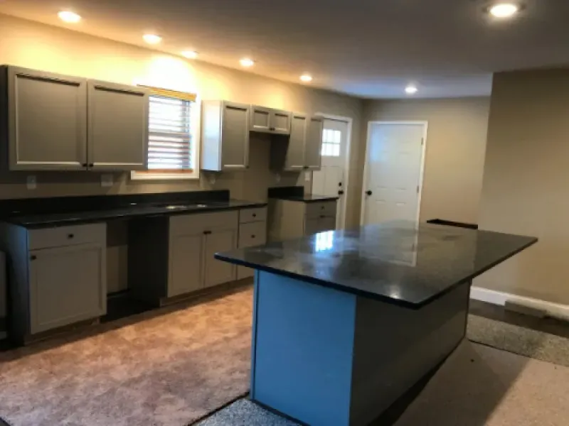 Empty kitchen with gray cabinets, black countertops, and a large center island under recessed lights