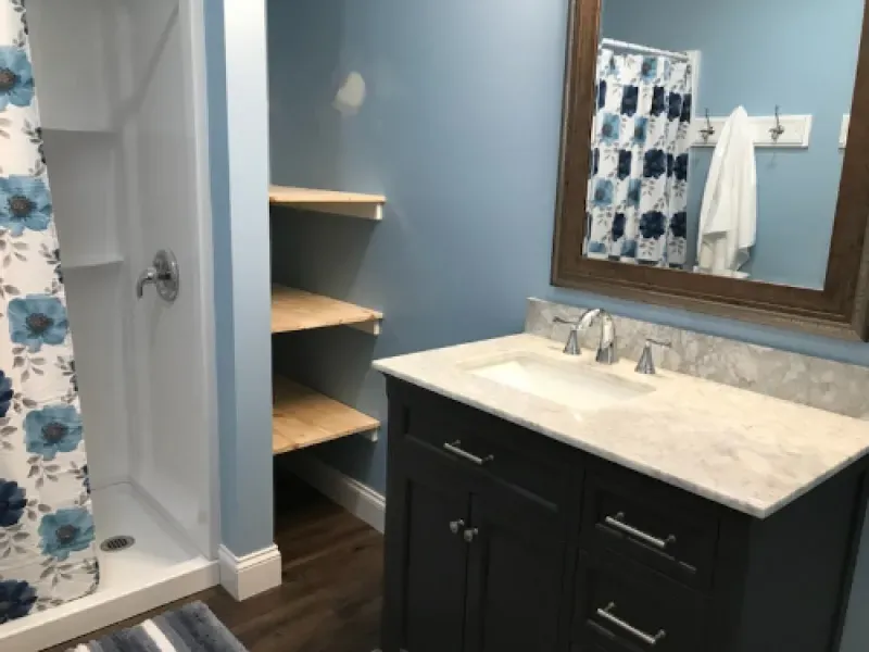 Modern bathroom with dark vanity, light countertop, blue walls, mirror, and open corner shelves