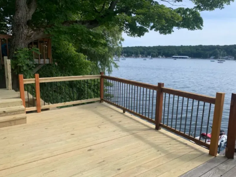 Wooden lakeside deck with railing overlooking calm water and distant boats