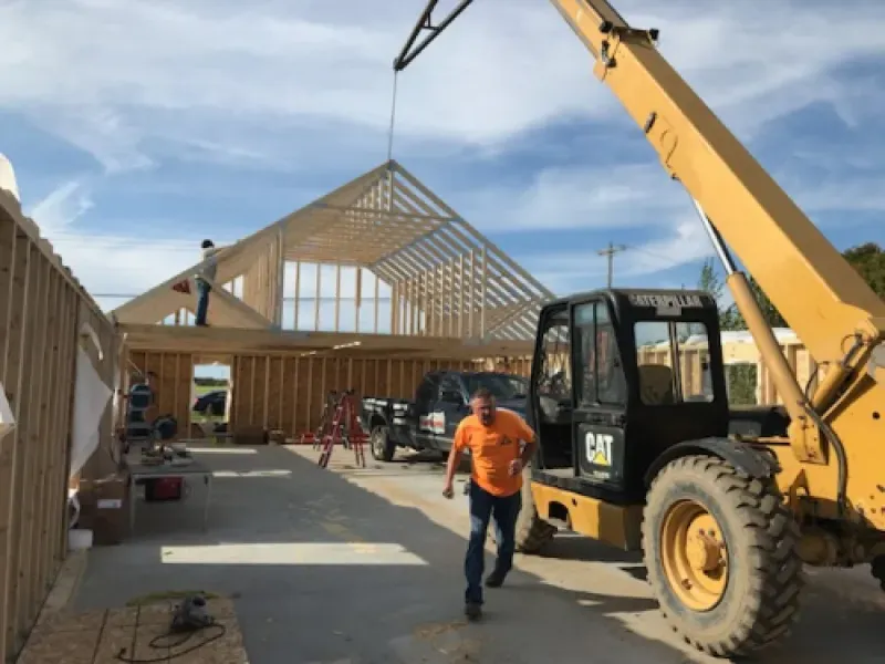 Construction site with workers, crane, and a wooden house frame under assembly