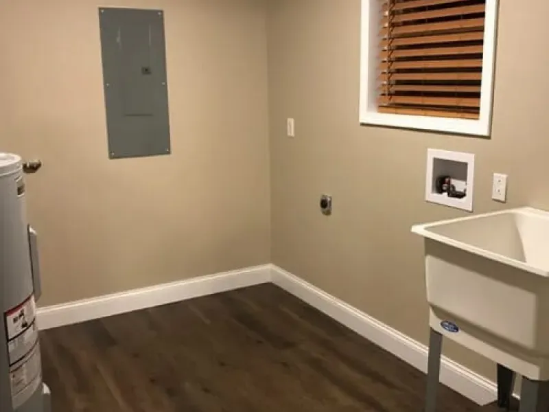 Empty utility room with sink, electrical panel, and window blinds on beige walls.