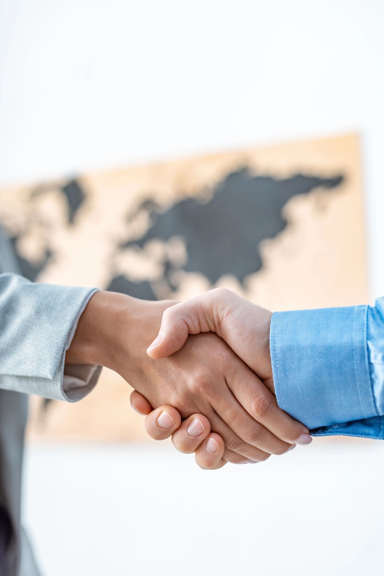 Dos personas se dan la mano, con un mapa del mundo borroso de fondo.