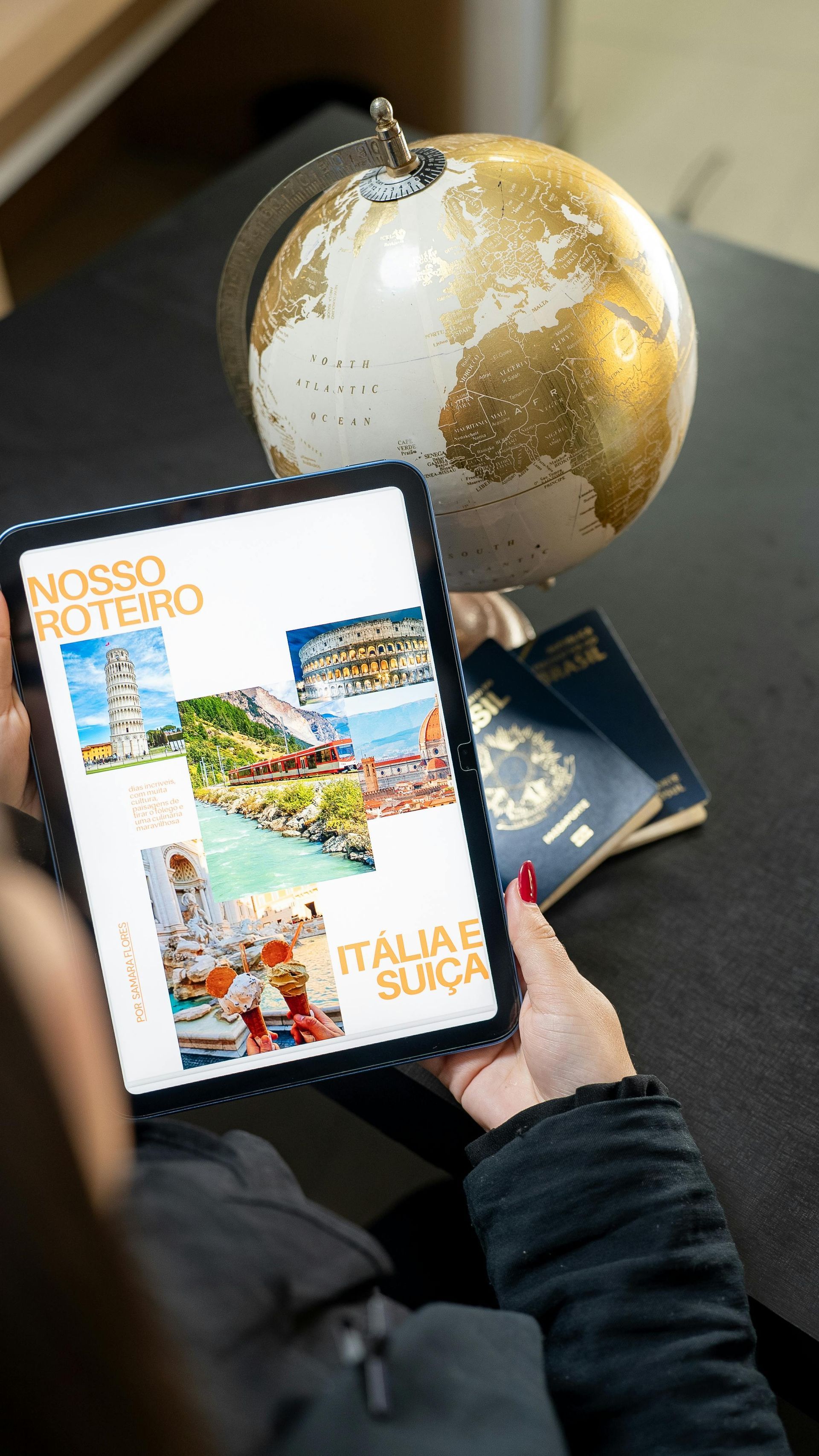 Persona sosteniendo una tableta con fotos de viajes, un globo terráqueo y pasaportes sobre una mesa.