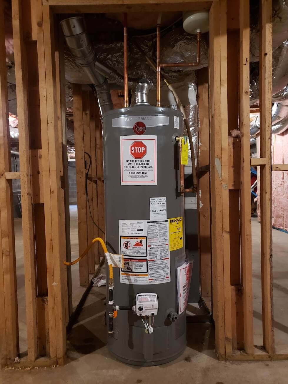A water heater is sitting in a basement surrounded by wooden walls.