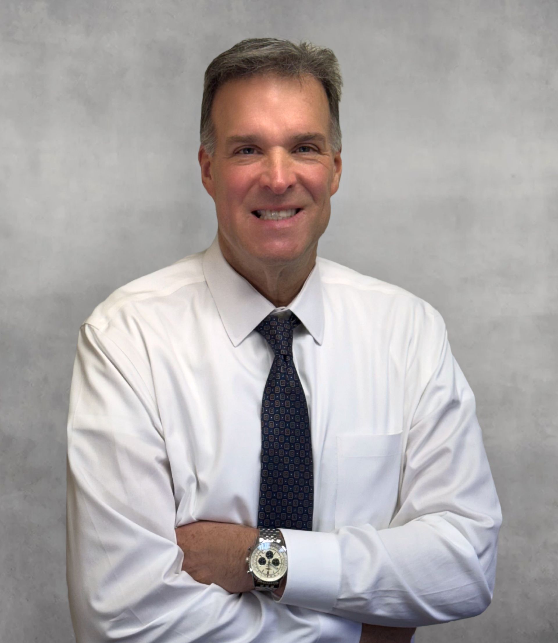 Man in a white shirt and tie, arms crossed, smiling, professional setting.