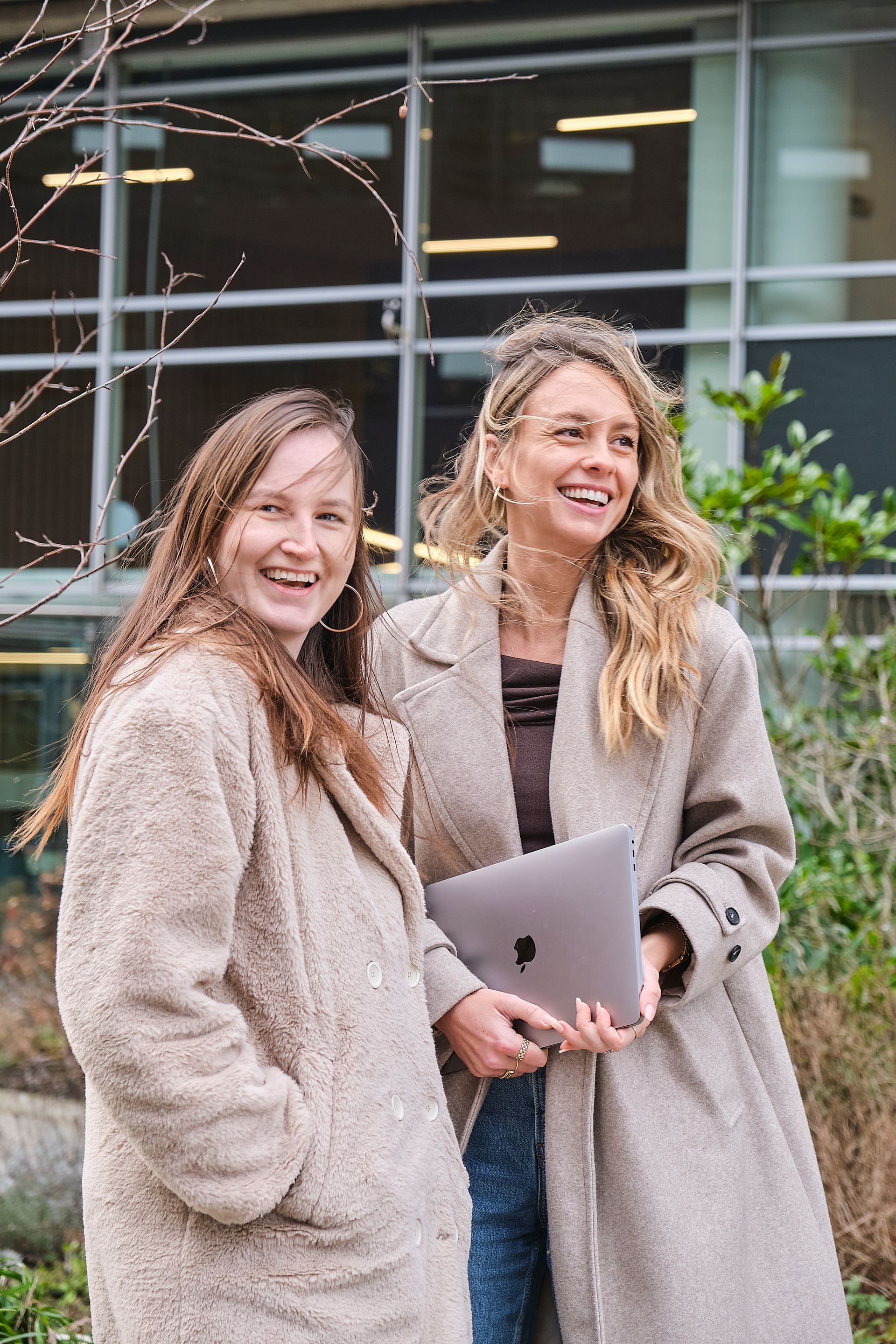Twee vrouwen staan naast elkaar voor een gebouw met een laptop in hun handen.