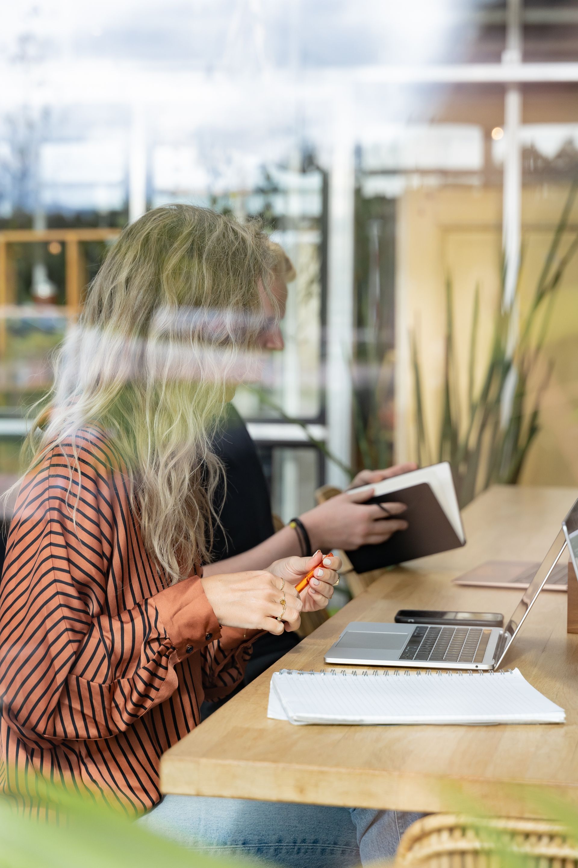 Person studying at a desk with a laptop and notebook in a glass-walled office