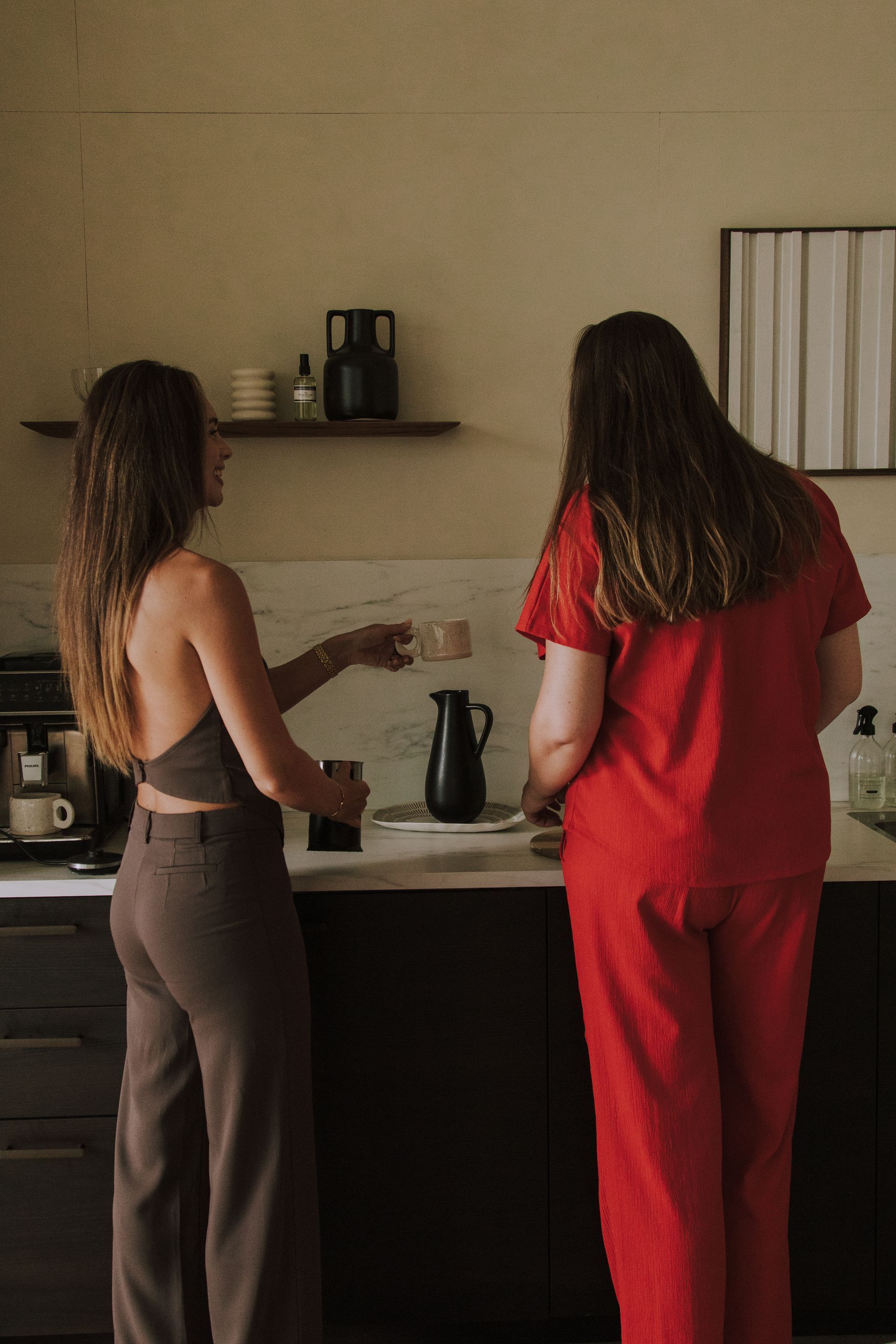 Two people standing at a kitchen counter, preparing drinks near a coffee machine.