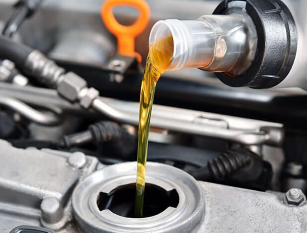 A close up of a person pouring oil into a car engine.