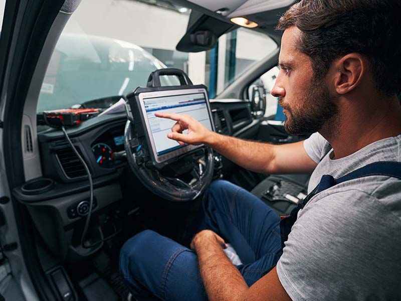 A man is sitting in the driver 's seat of a car using a tablet.