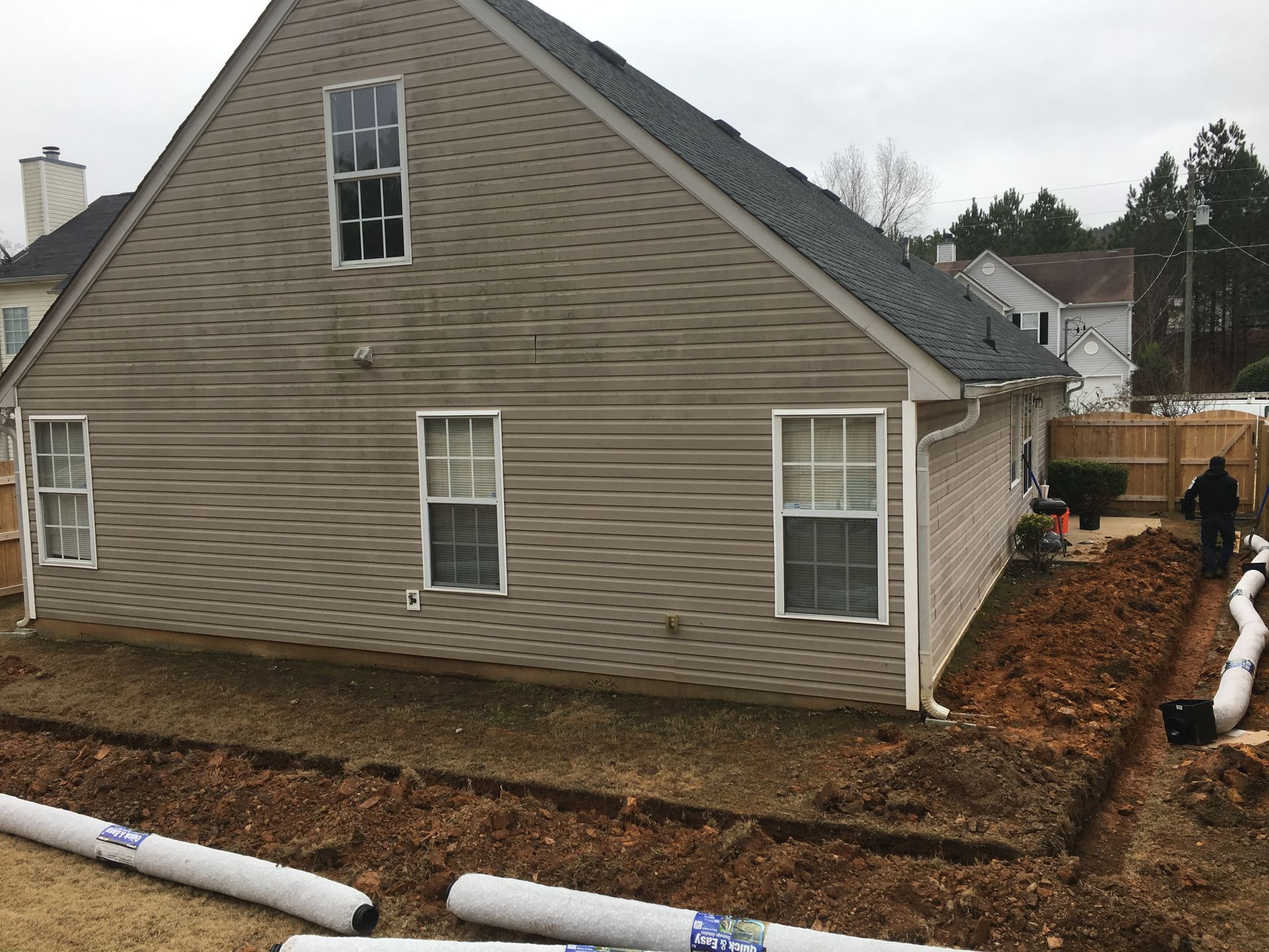House with new drainage pipes installed along a muddy yard under overcast skies