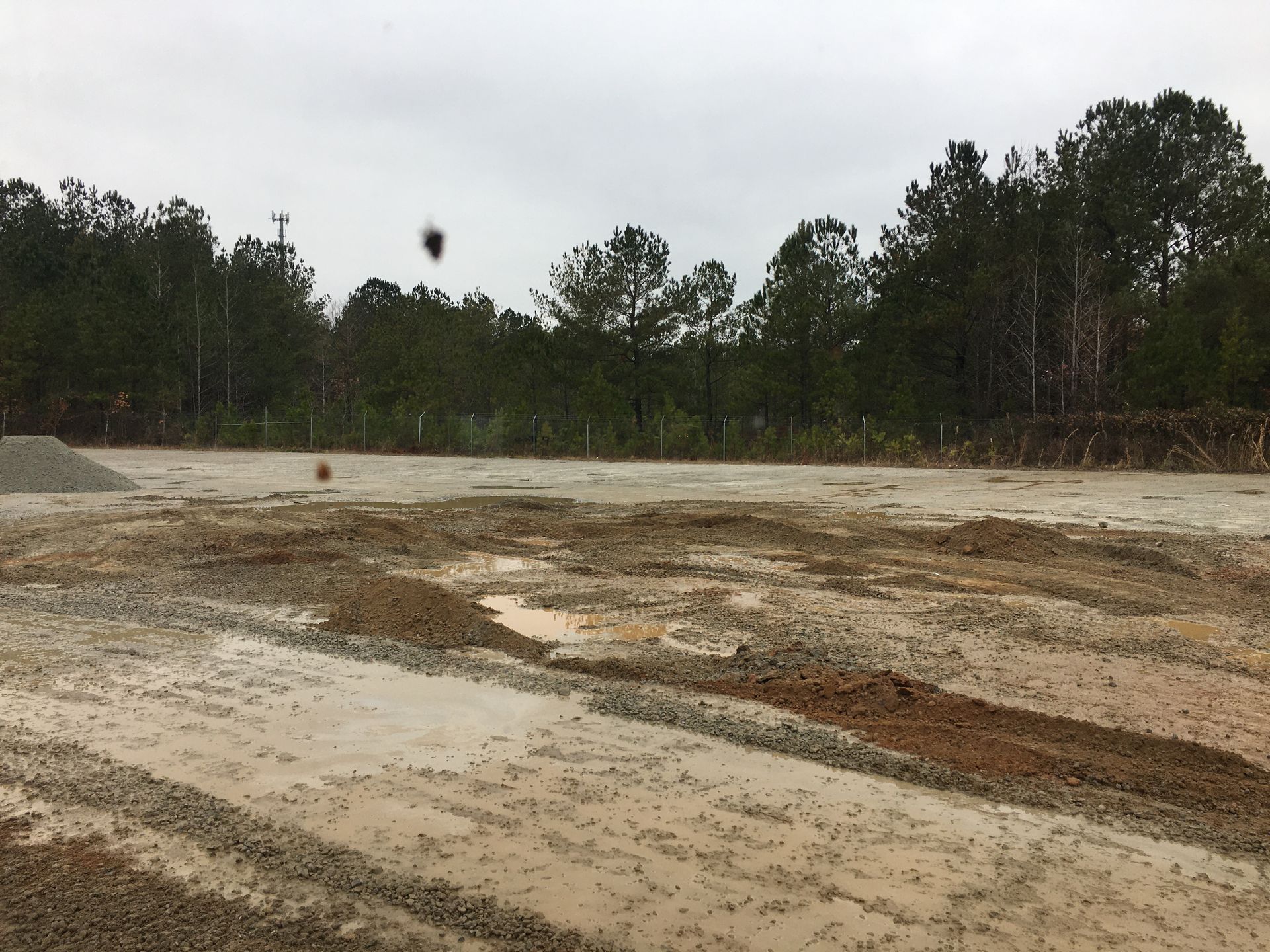 A muddy field with trees in the background on a cloudy day