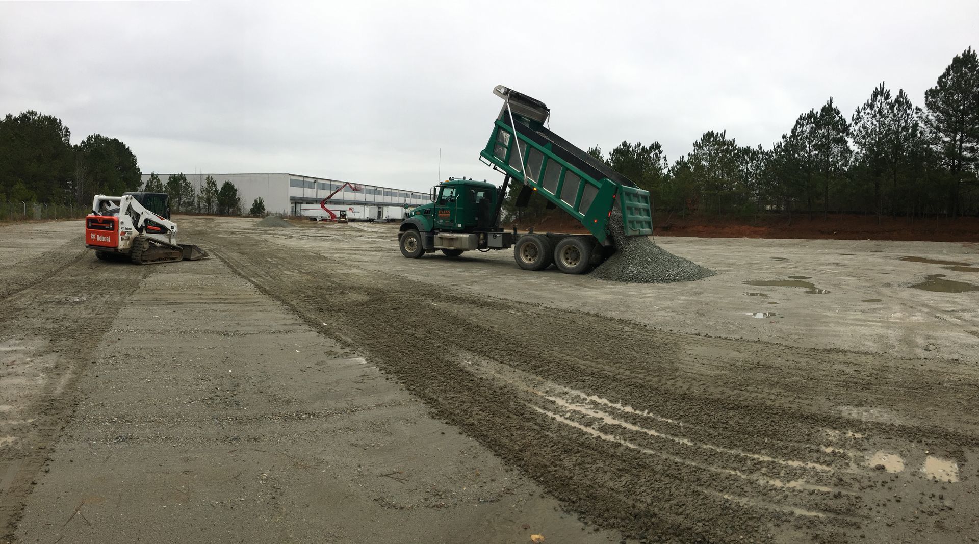 A dump truck is being loaded with gravel in a dirt field.