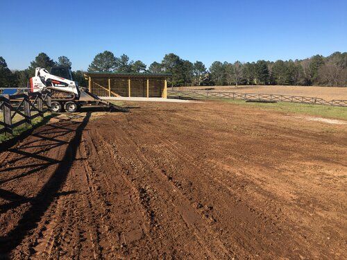 A bulldozer is sitting on top of a dirt field next to a fence.