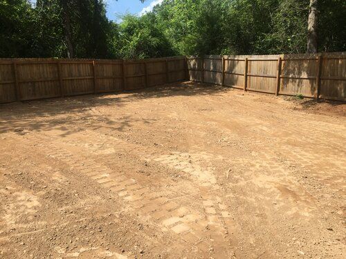 A dirt yard with a wooden fence and trees in the background.