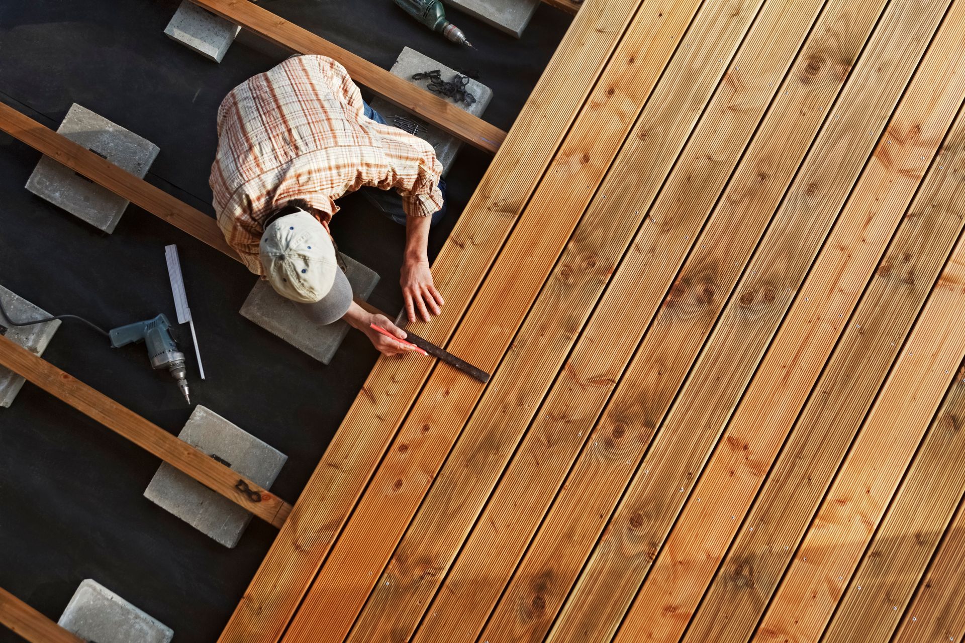 Person installing wooden deck boards with tools, high-angle view.