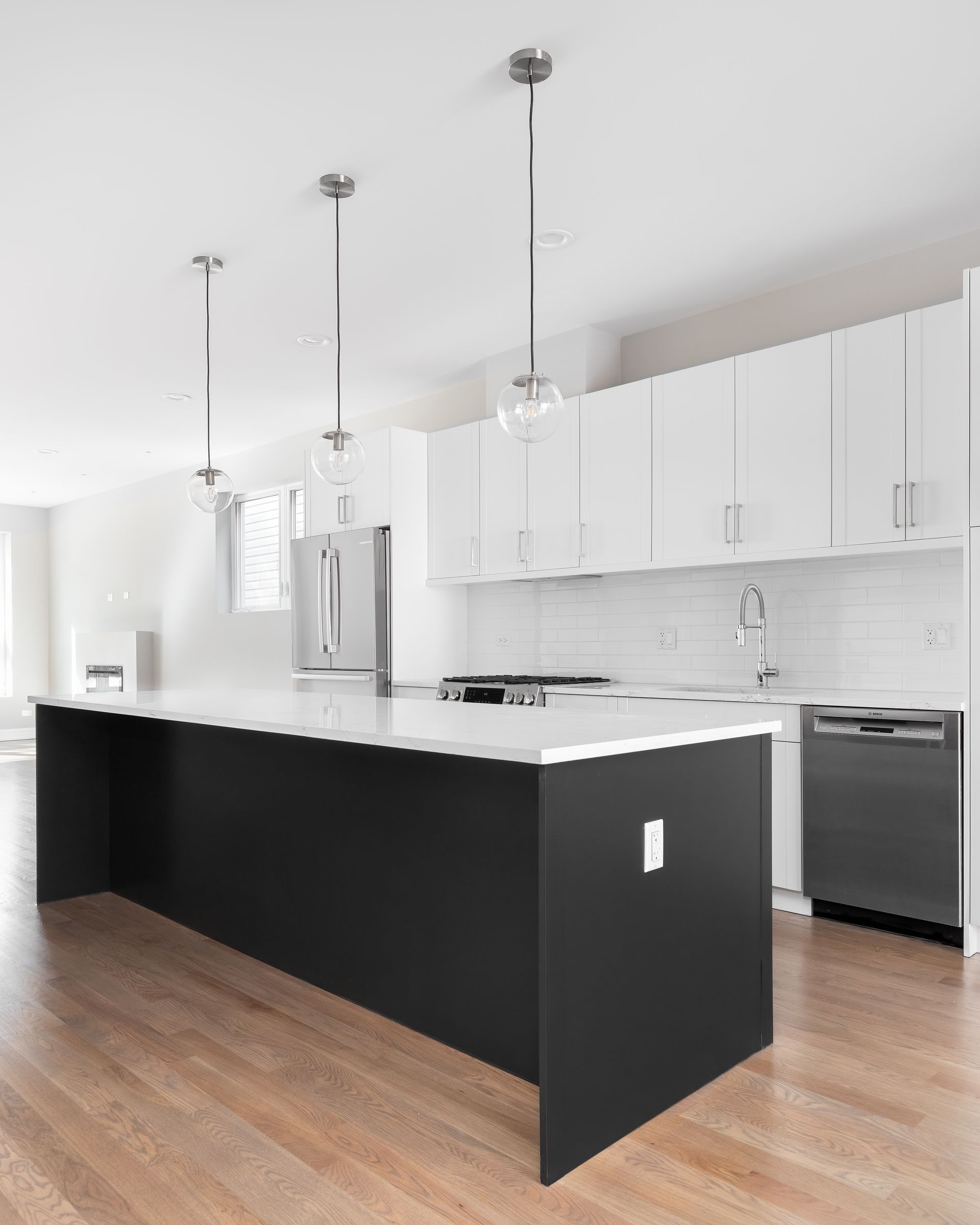 Modern kitchen with black island, white countertops, stainless steel appliances, and wood floor.