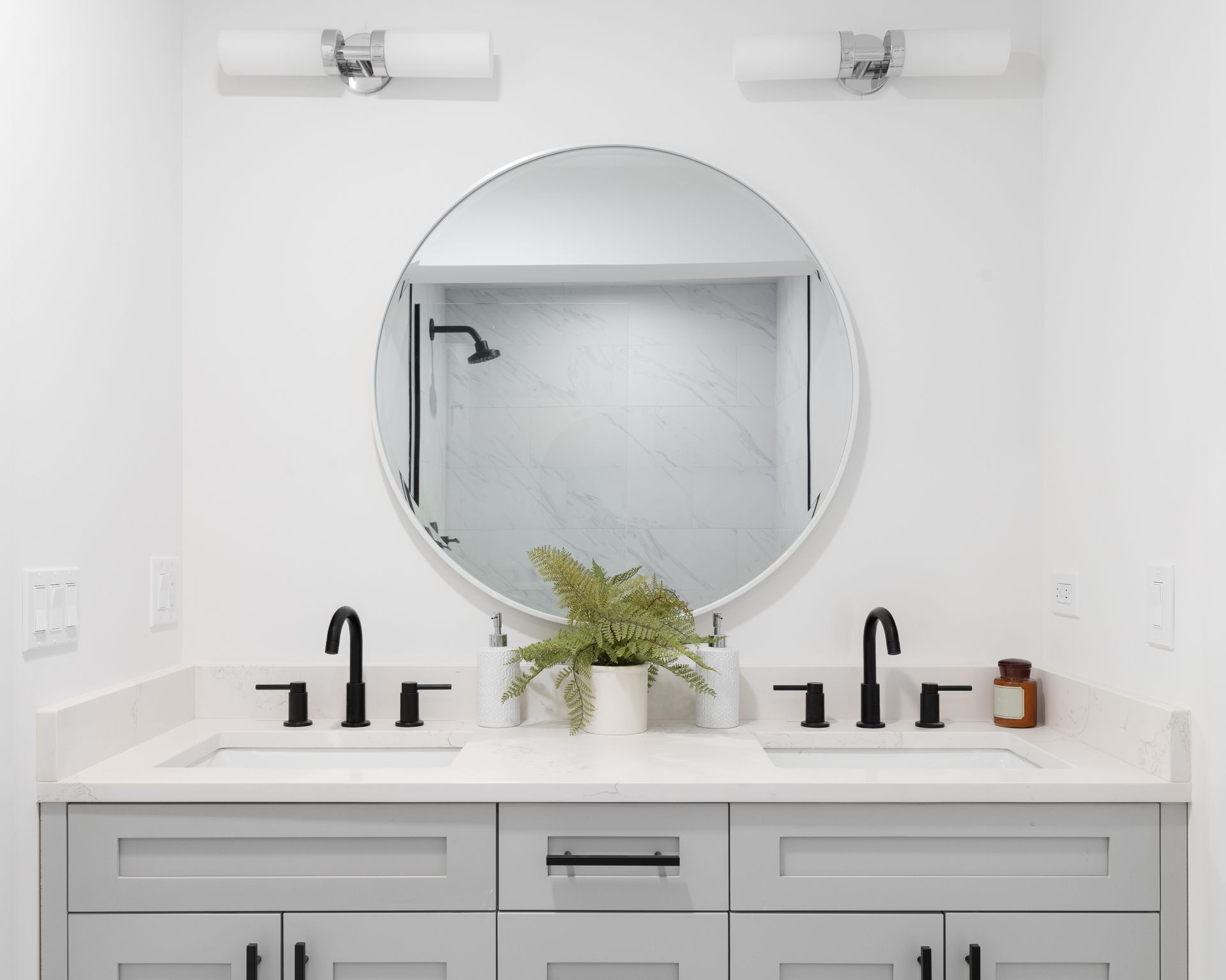 Bathroom with double vanity, round mirror, and black fixtures.