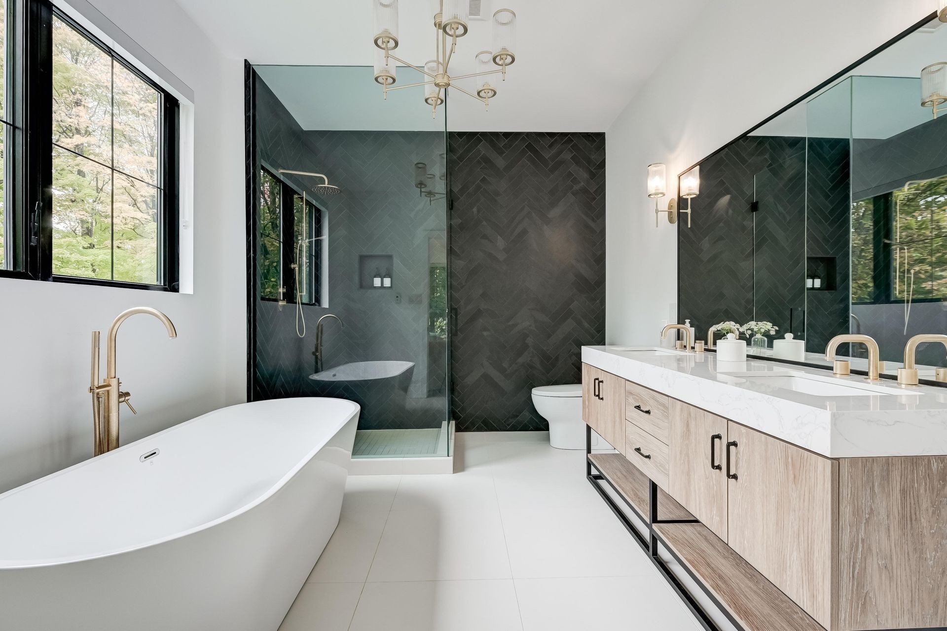Modern bathroom with white tub, double vanity, and glass shower; gold fixtures, dark accent wall.