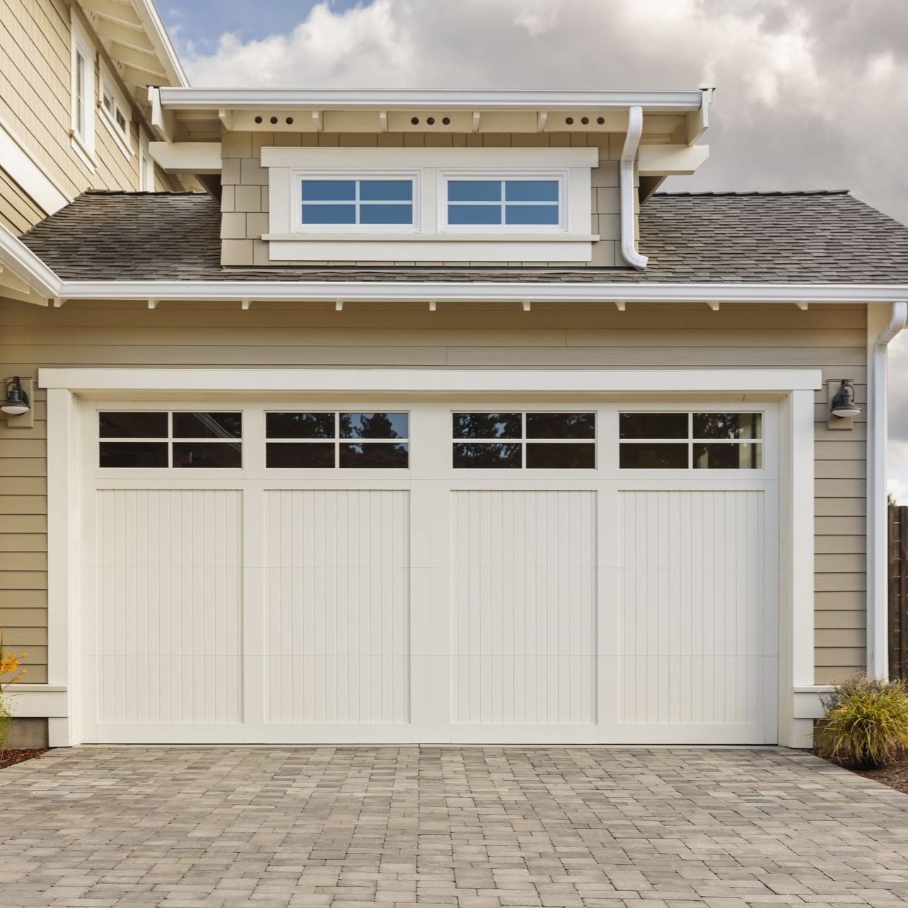 White garage door with windows, tan siding, and brick driveway.