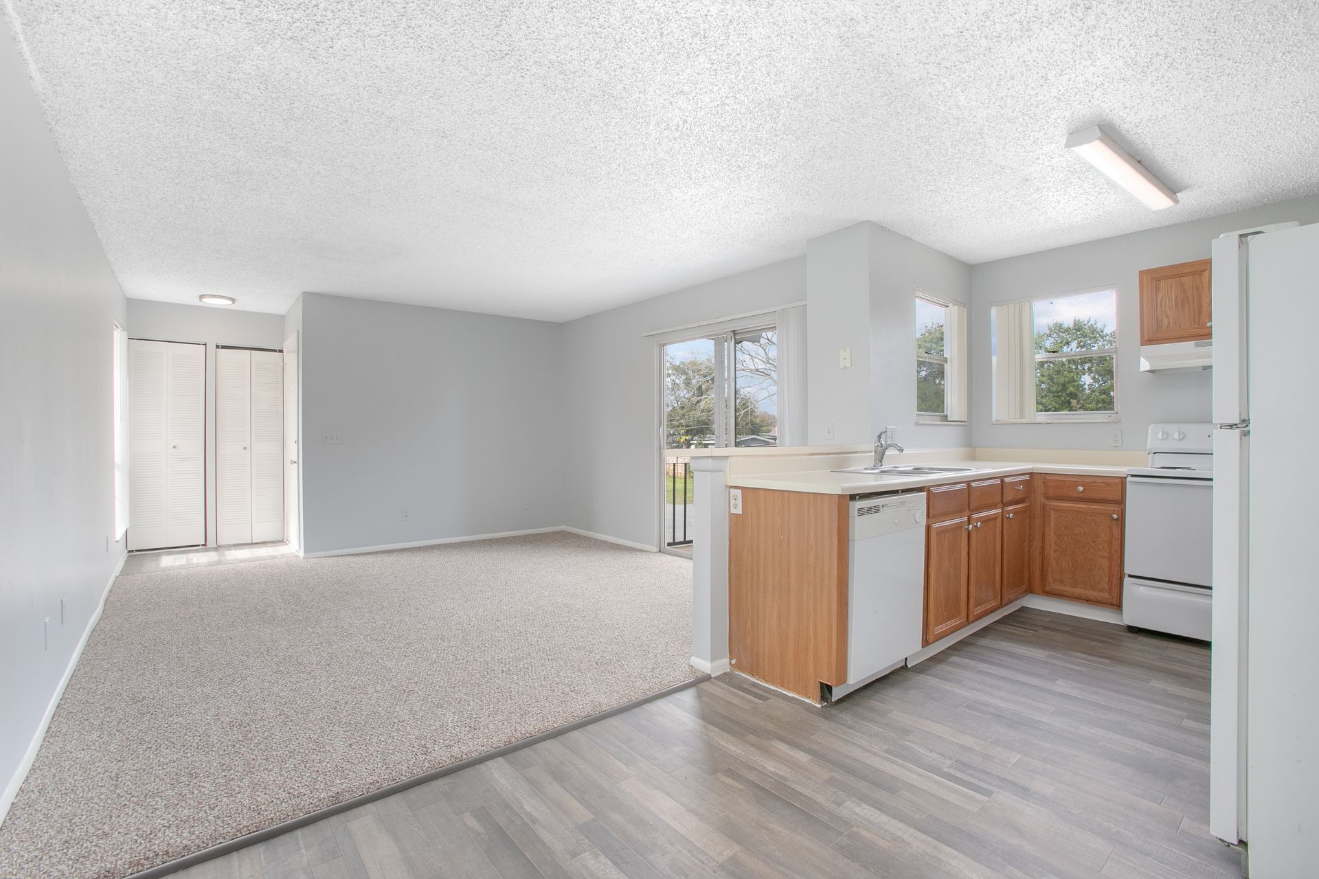 Empty apartment kitchen and living room with gray flooring, white walls, and natural light
