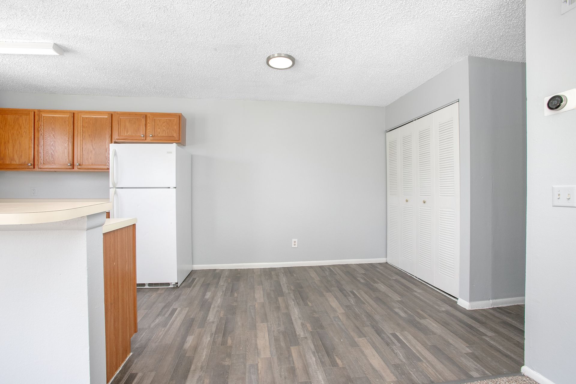 Empty kitchen with gray walls, wood-look flooring, white refrigerator, and closet doors.