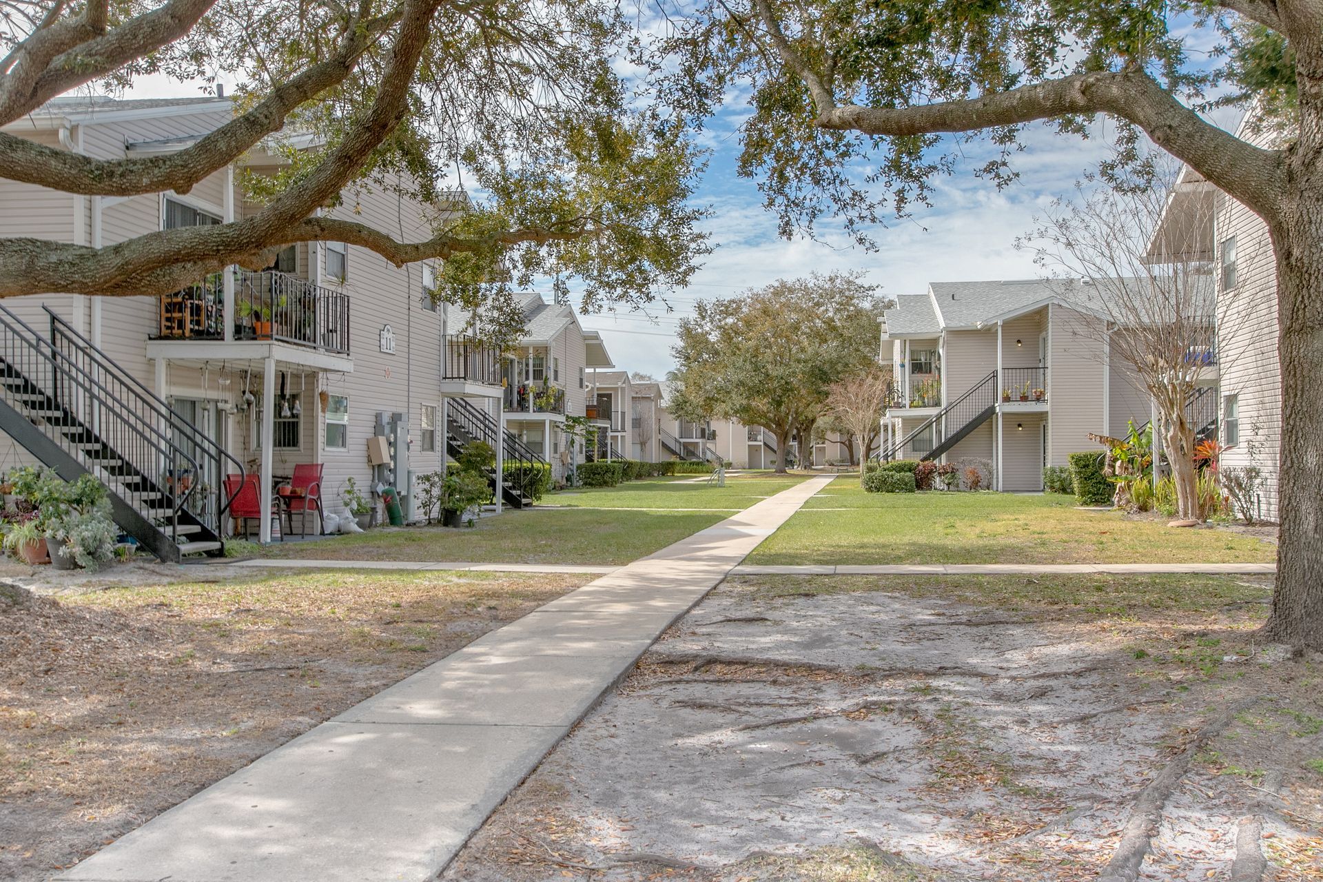 Apartment complex courtyard with concrete paths, white buildings, and large trees on both sides