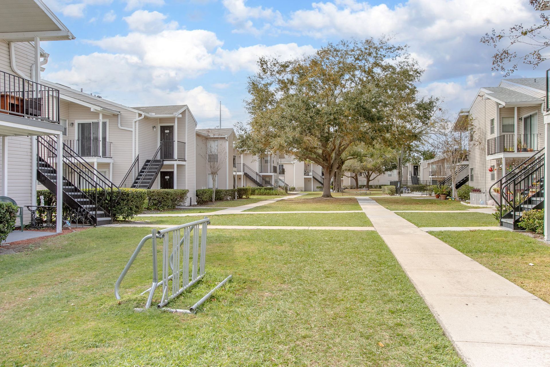 Apartment courtyard with grass, sidewalk, and multi-story buildings under a partly cloudy sky