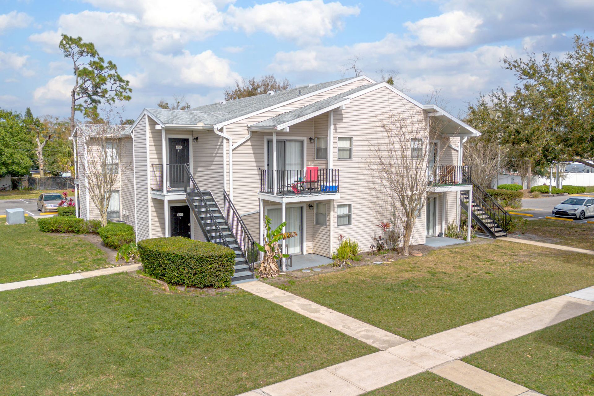Two-story beige apartment building with stairs, balconies, and a grassy courtyard under a blue sky