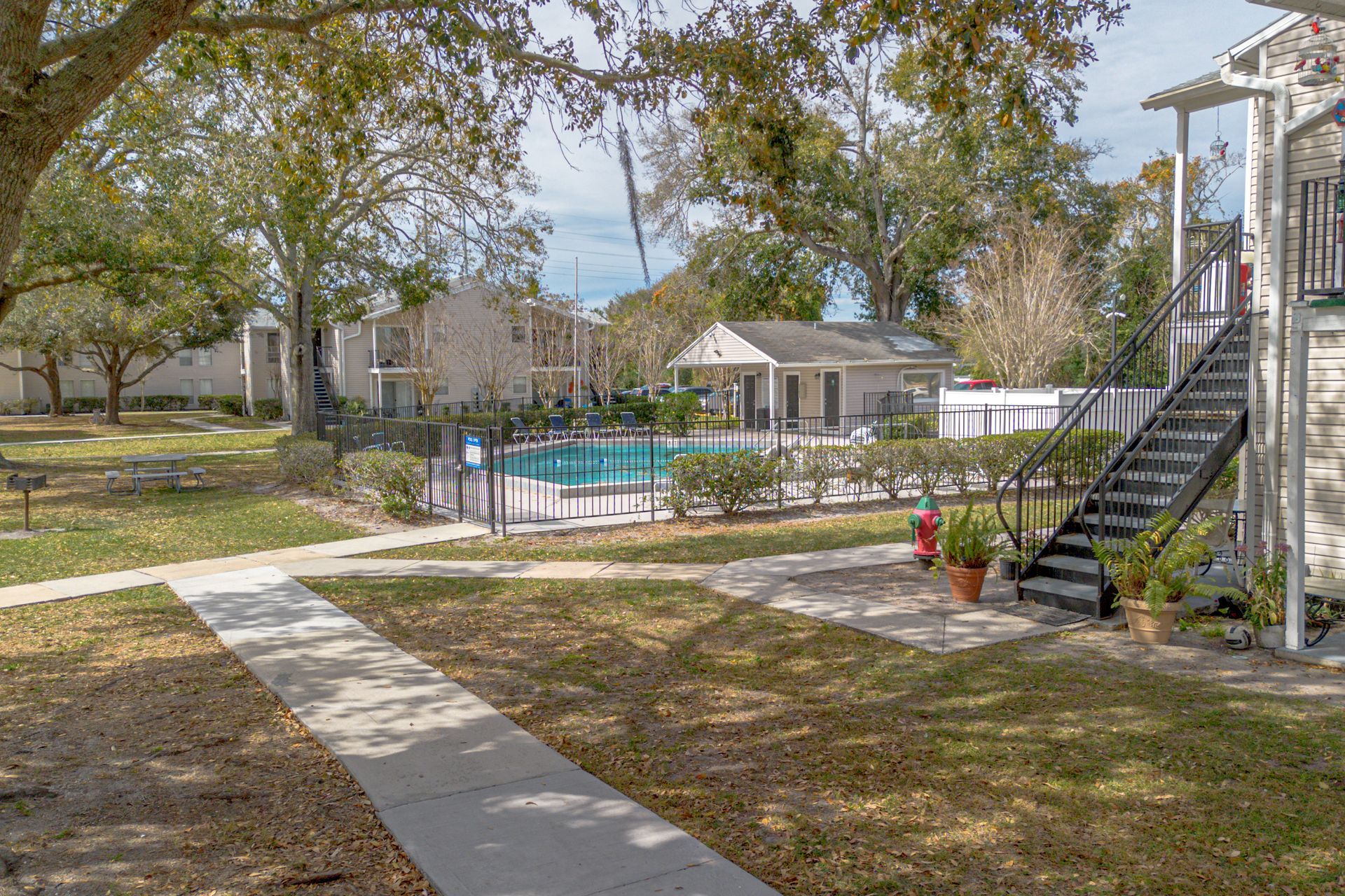 Apartment complex courtyard with a swimming pool, lawn, walkway, and staircase under trees