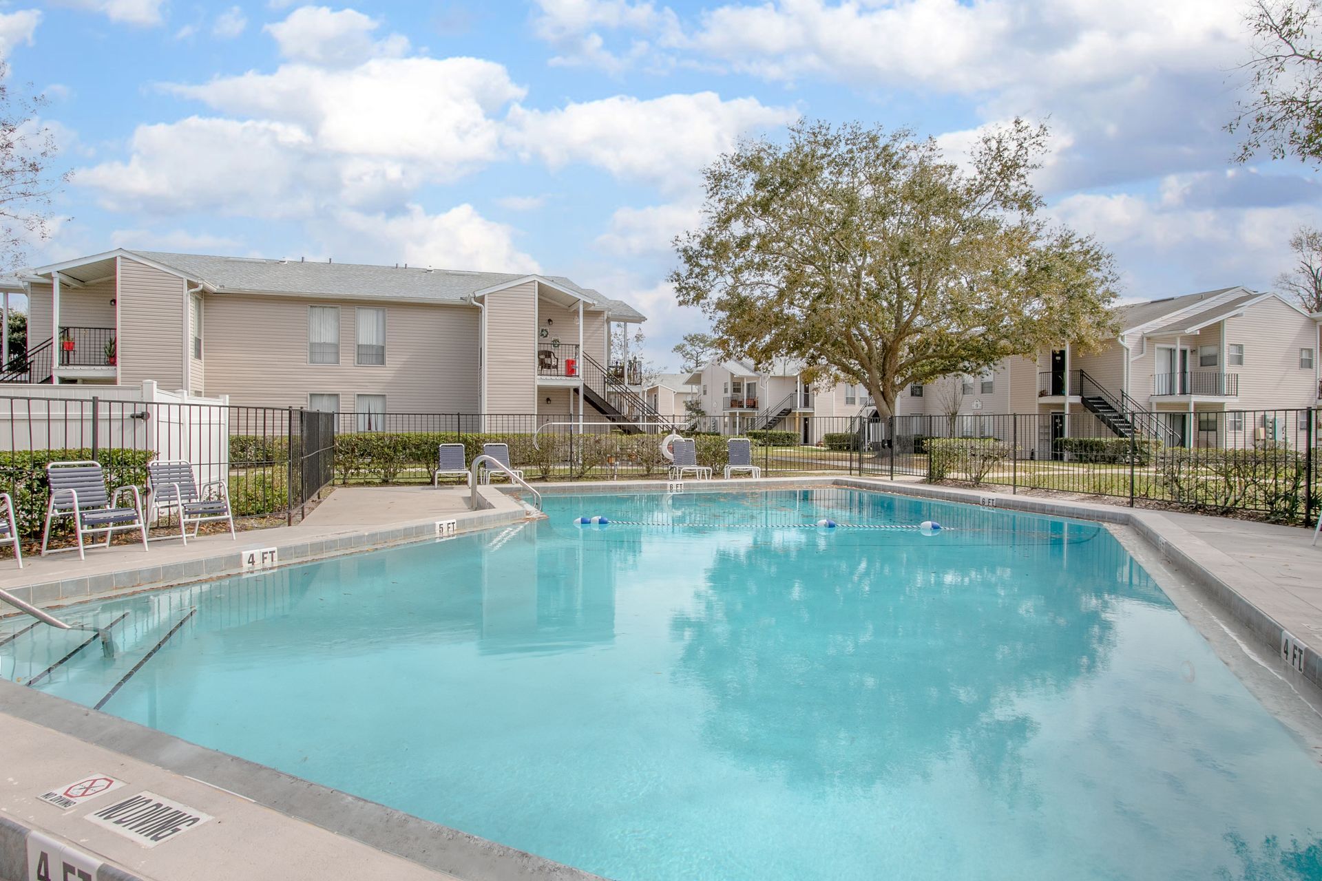 Apartment complex pool with turquoise water, lounge chairs, and a partly cloudy sky