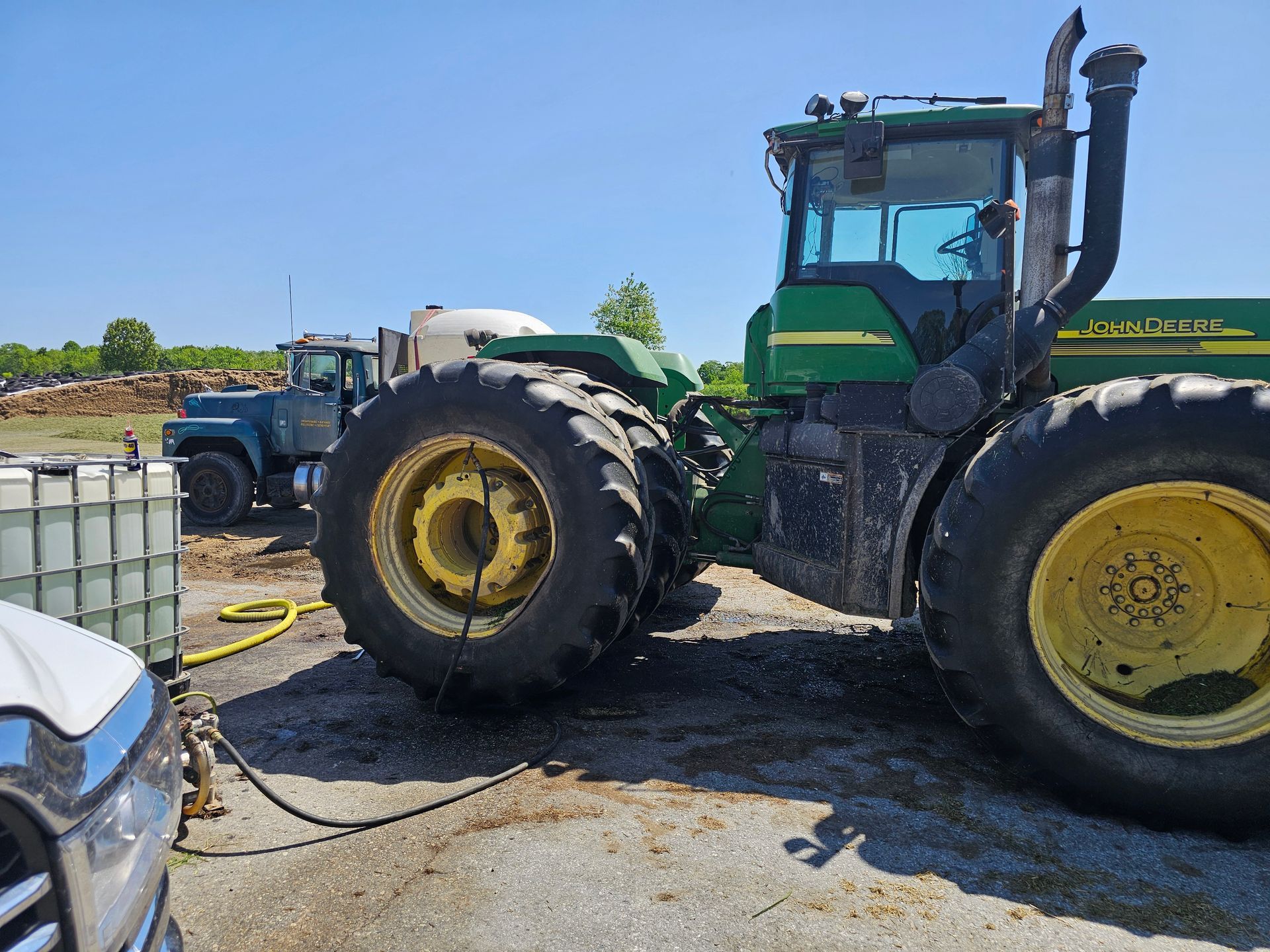 A green and yellow john deere tractor is parked next to a truck.