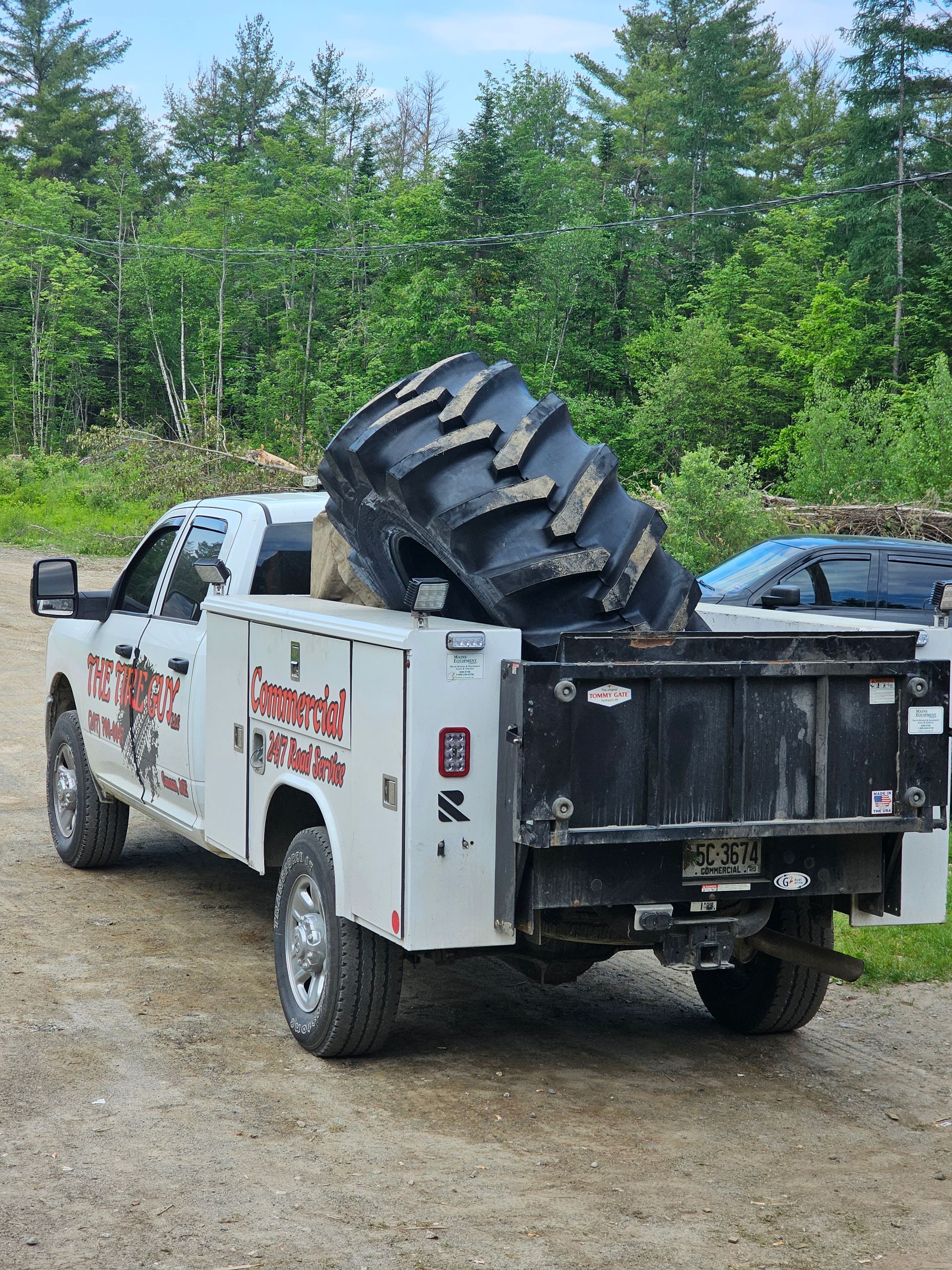 A tow truck with a large tire in the back is parked on a dirt road.